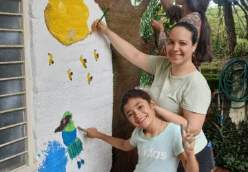 Madre e hija pintando juntas un árbol y aves durante la jornada de integración familiar y educación alternativa.