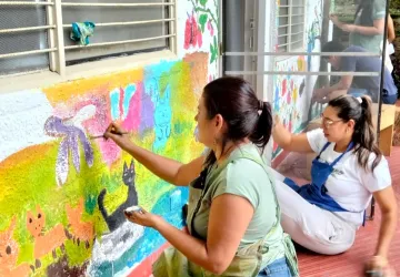 Madres de familia pintando animales y naturaleza en la fachada, embelleciendo el entorno de los niños.